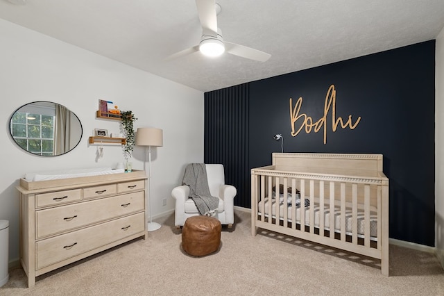 bedroom featuring a textured ceiling, ceiling fan, a crib, and light carpet