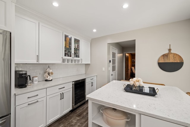 kitchen featuring backsplash, wine cooler, stainless steel fridge, light stone counters, and white cabinetry