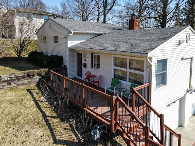 back of property featuring a wooden deck, a yard, a chimney, and a shingled roof