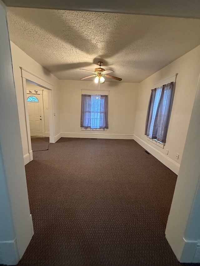 empty room featuring ceiling fan, dark carpet, and a textured ceiling