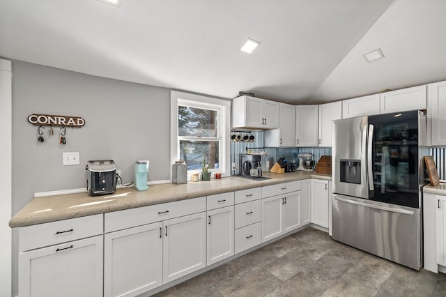 kitchen featuring lofted ceiling, stainless steel fridge, white cabinetry, and backsplash