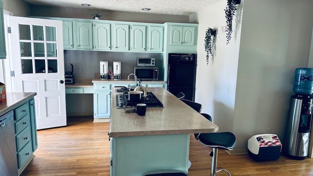 920 Woodbine St, Willard, OH 44890 - kitchen with appliances with stainless steel finishes, light wood finished floors, a kitchen breakfast bar, a kitchen island, and a textured ceiling