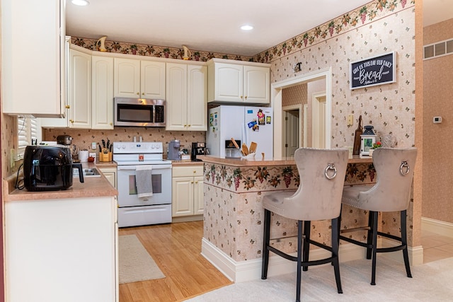 kitchen featuring a kitchen bar, white cabinetry, light hardwood / wood-style floors, and white appliances