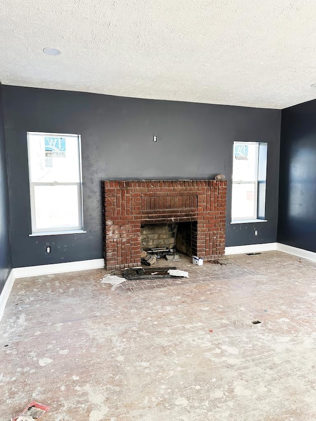 unfurnished living room featuring a textured ceiling, a wealth of natural light, and a brick fireplace