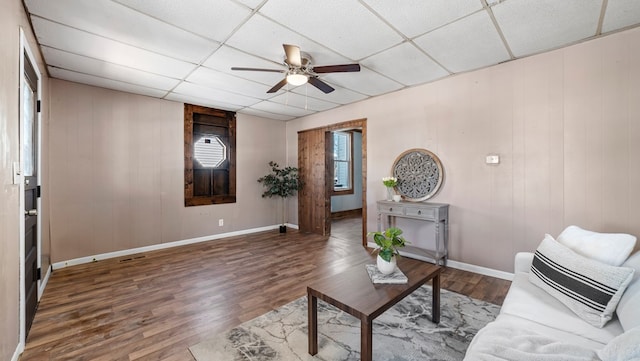 living room with dark hardwood / wood-style floors, a drop ceiling, and ceiling fan