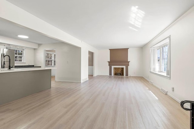 unfurnished living room featuring a fireplace with flush hearth, light wood-style flooring, baseboards, and a sink