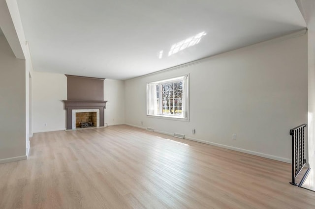 unfurnished living room featuring light wood finished floors, a fireplace with flush hearth, baseboards, and visible vents