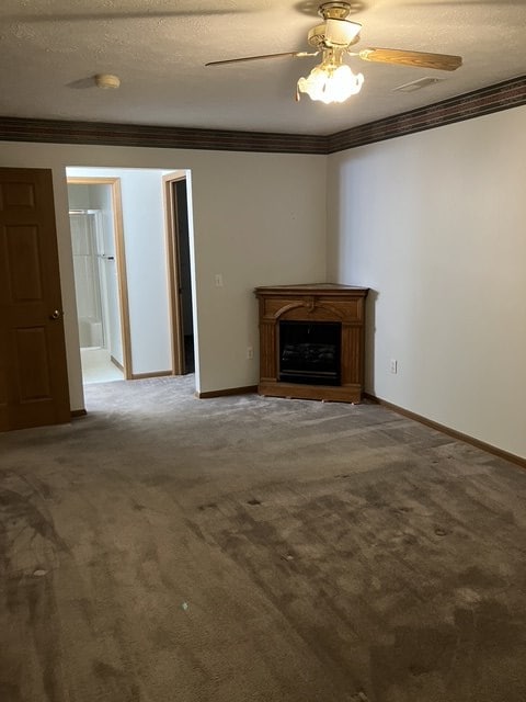 unfurnished living room featuring carpet, a textured ceiling, ceiling fan, and ornamental molding