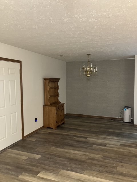 unfurnished dining area with dark hardwood / wood-style flooring, a textured ceiling, and an inviting chandelier