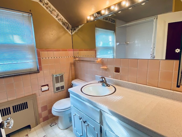 bathroom with toilet, heating unit, radiator heating unit, vanity, and a wealth of natural light