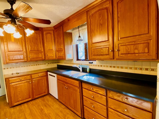 kitchen featuring sink, decorative light fixtures, white dishwasher, light hardwood / wood-style floors, and backsplash