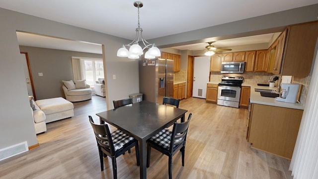 dining space featuring sink, ceiling fan with notable chandelier, and light hardwood / wood-style flooring