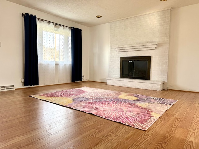 unfurnished living room featuring a brick fireplace, wood-type flooring, visible vents, and a textured ceiling