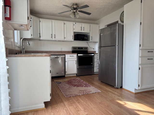 kitchen with light wood finished floors, appliances with stainless steel finishes, a ceiling fan, white cabinetry, and a sink