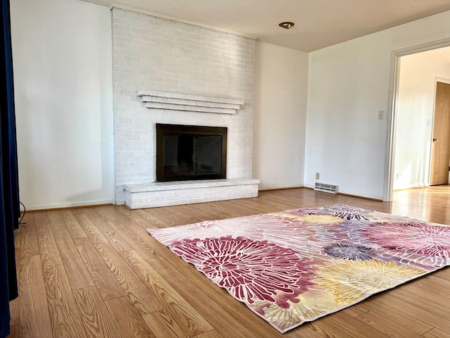 living room featuring a brick fireplace, visible vents, baseboards, and wood finished floors