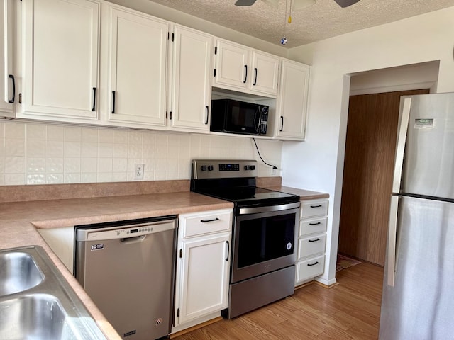 kitchen featuring white cabinets, light countertops, appliances with stainless steel finishes, light wood-type flooring, and decorative backsplash