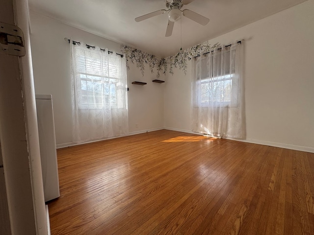 empty room featuring wood-type flooring, a ceiling fan, and baseboards