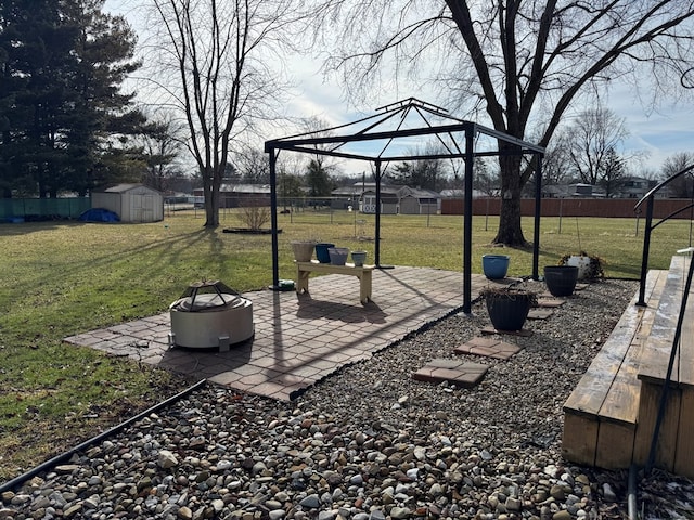 view of yard featuring a fire pit, a storage shed, an outdoor structure, fence, and a gazebo