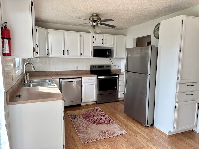 kitchen with light wood-style flooring, a sink, a ceiling fan, white cabinets, and appliances with stainless steel finishes