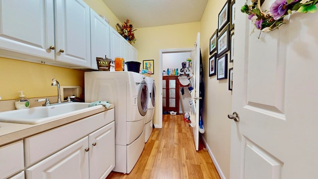 clothes washing area with sink, light hardwood / wood-style flooring, cabinets, a textured ceiling, and washing machine and clothes dryer