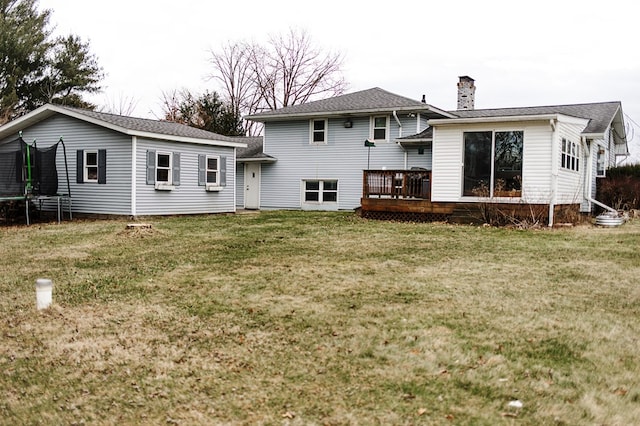 rear view of property with a yard, a trampoline, a chimney, and a wooden deck