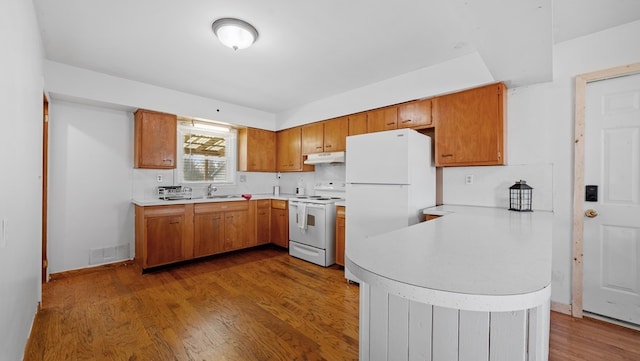 kitchen featuring sink, dark hardwood / wood-style flooring, backsplash, kitchen peninsula, and white appliances