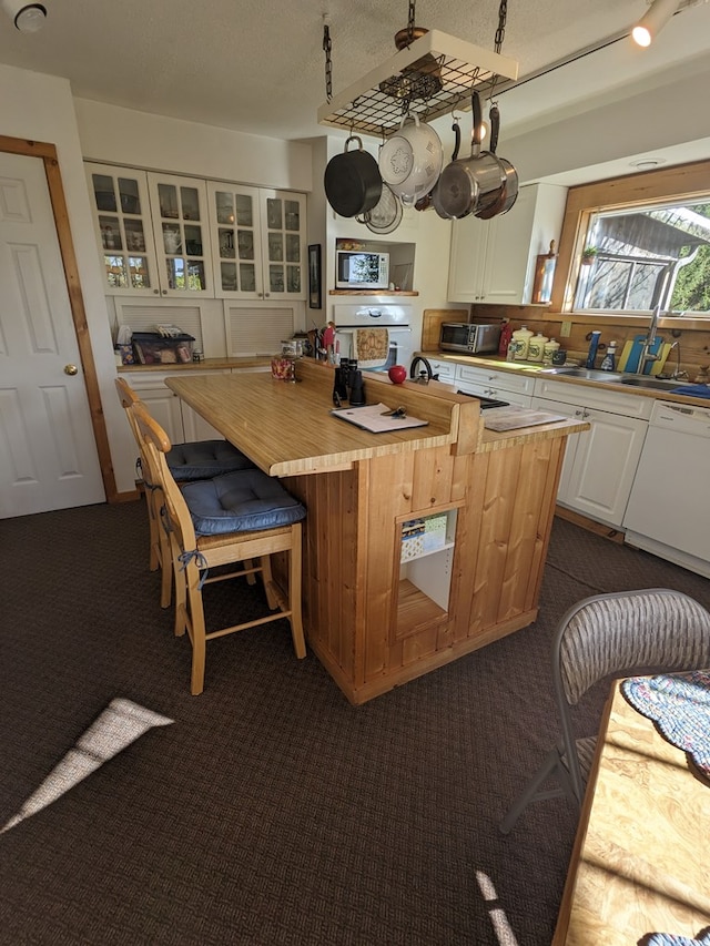 kitchen with dark colored carpet, dishwasher, white cabinets, and a kitchen island