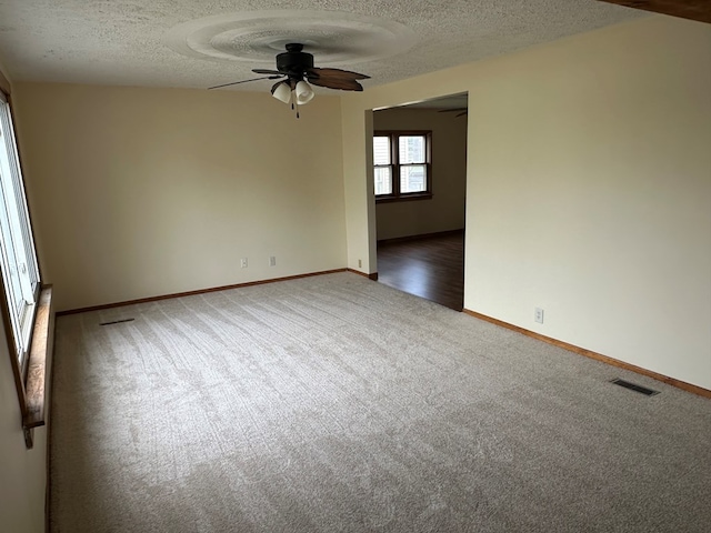 carpeted spare room with ceiling fan, a textured ceiling, baseboards, and visible vents