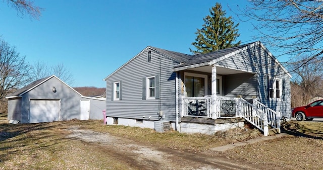 bungalow-style house with a detached garage, an outbuilding, covered porch, and dirt driveway