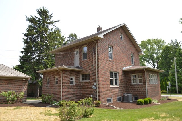 1211 S Sandusky Ave, Bucyrus, OH 44820 - back of house with central AC, brick siding, a chimney, and a lawn
