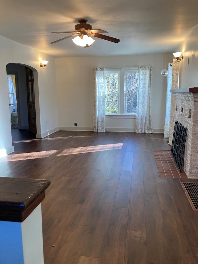 unfurnished living room featuring ceiling fan, dark hardwood / wood-style flooring, and a brick fireplace