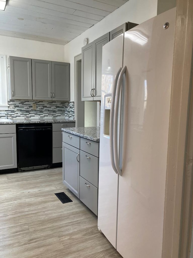 kitchen featuring dishwasher, white fridge with ice dispenser, light stone counters, gray cabinets, and decorative backsplash