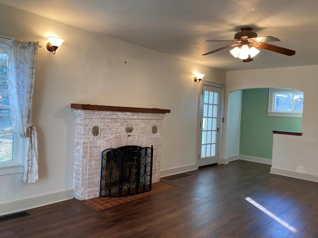 unfurnished living room featuring ceiling fan, plenty of natural light, dark hardwood / wood-style floors, and a brick fireplace