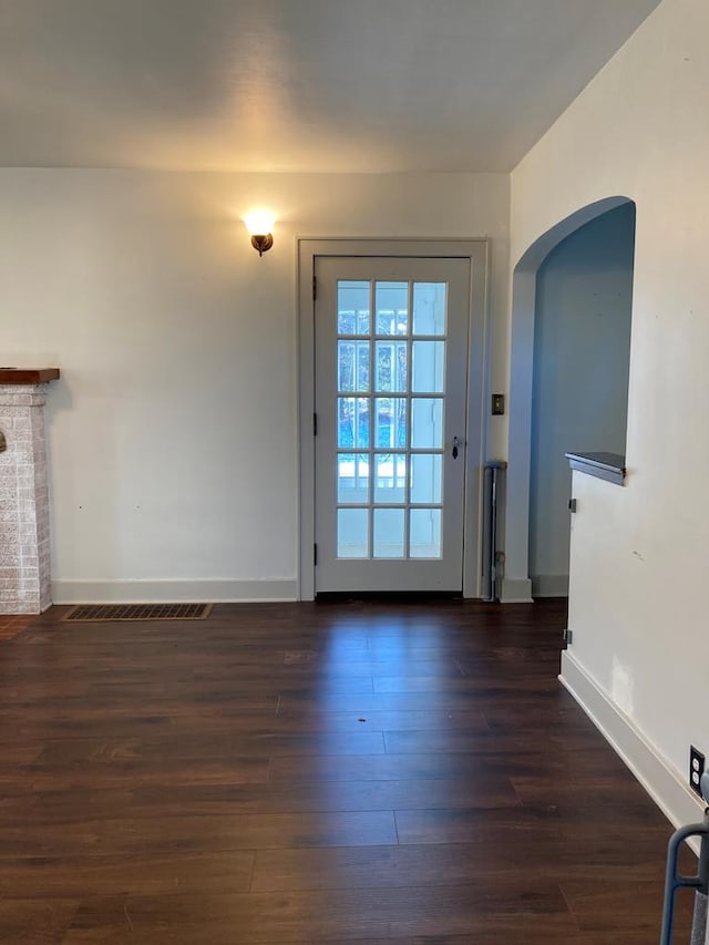 doorway with a fireplace and dark wood-type flooring