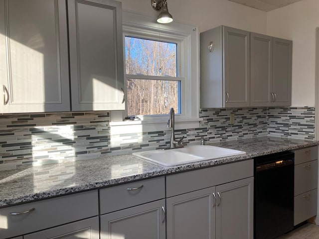 kitchen featuring black dishwasher, light stone counters, gray cabinetry, and sink