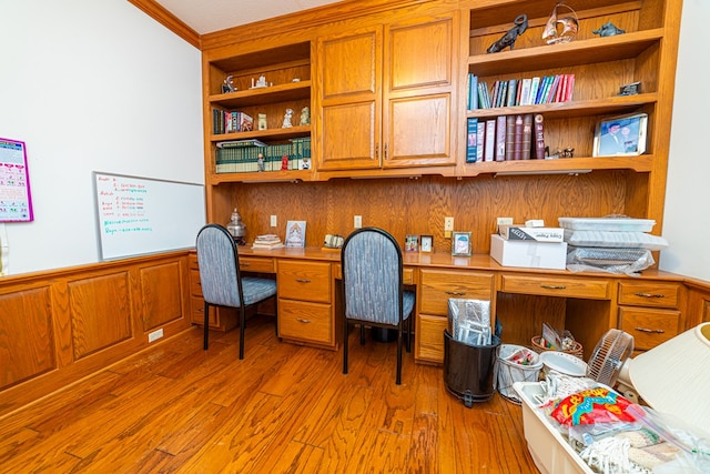 office featuring light wood-type flooring, built in desk, crown molding, and wooden walls