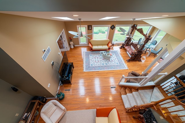 living room featuring a towering ceiling, light wood-type flooring, a skylight, and ceiling fan