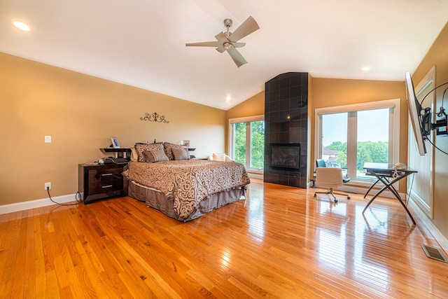 bedroom with hardwood / wood-style floors, ceiling fan, lofted ceiling, and a tiled fireplace