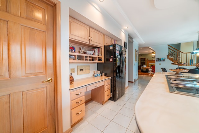 kitchen with black fridge, ornamental molding, light brown cabinets, built in desk, and light tile patterned flooring