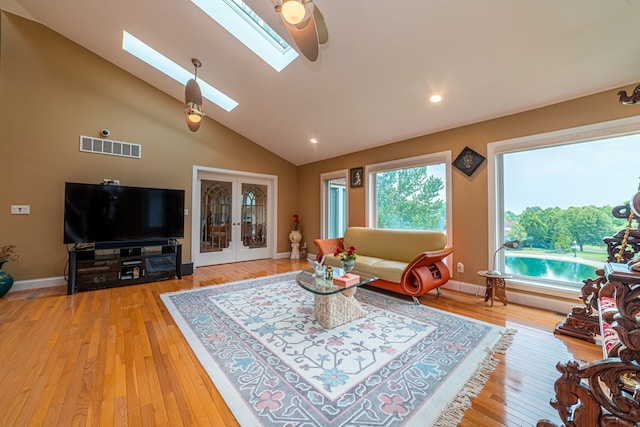 living room featuring french doors, light wood-type flooring, lofted ceiling with skylight, and ceiling fan