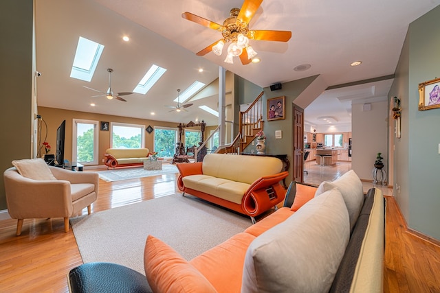 living room with ceiling fan, a skylight, high vaulted ceiling, and light hardwood / wood-style flooring