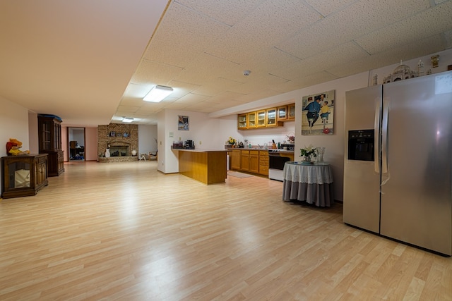 kitchen featuring white stove, a fireplace, light hardwood / wood-style floors, and stainless steel refrigerator with ice dispenser