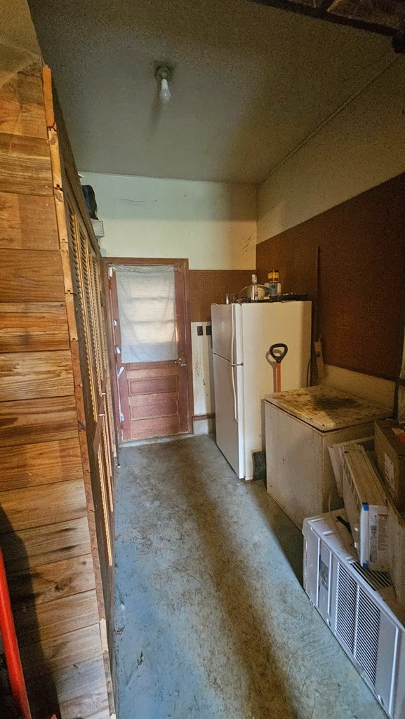 kitchen featuring white refrigerator, wooden walls, and concrete flooring