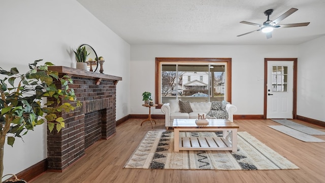 living room with ceiling fan, a brick fireplace, hardwood / wood-style floors, and a textured ceiling