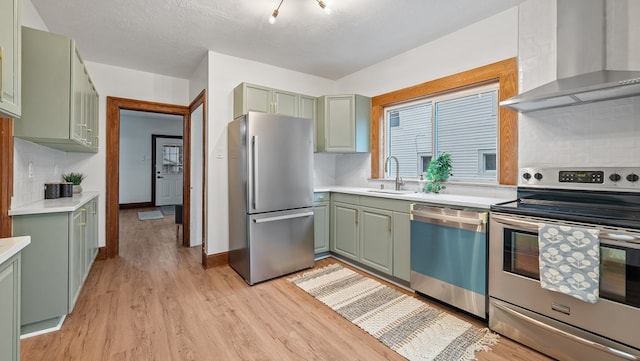 kitchen featuring sink, stainless steel appliances, light hardwood / wood-style floors, decorative backsplash, and wall chimney range hood