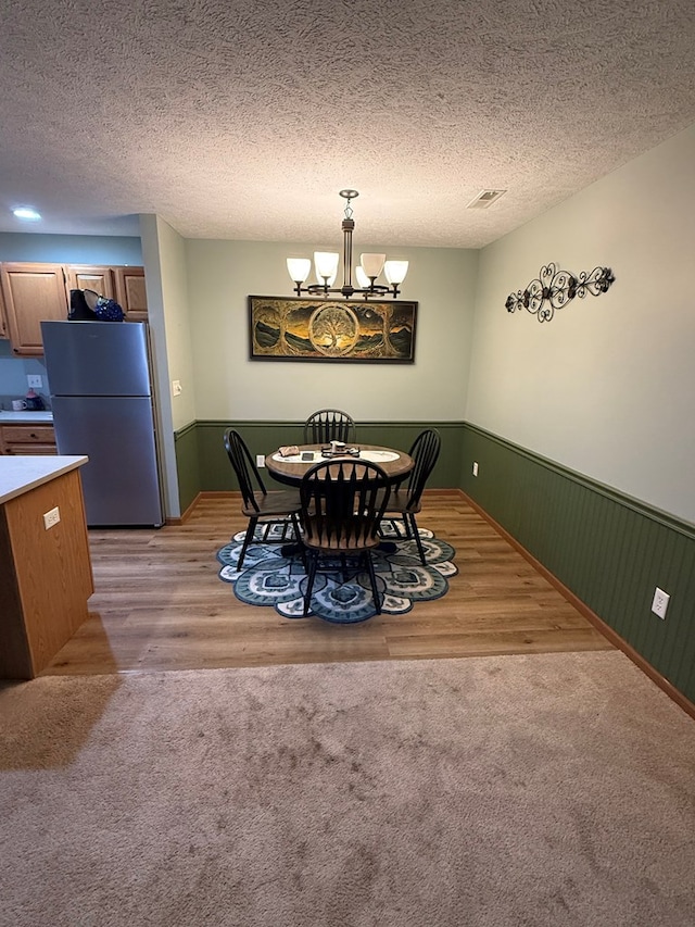 dining area featuring a wainscoted wall, a textured ceiling, visible vents, an inviting chandelier, and light wood-style flooring