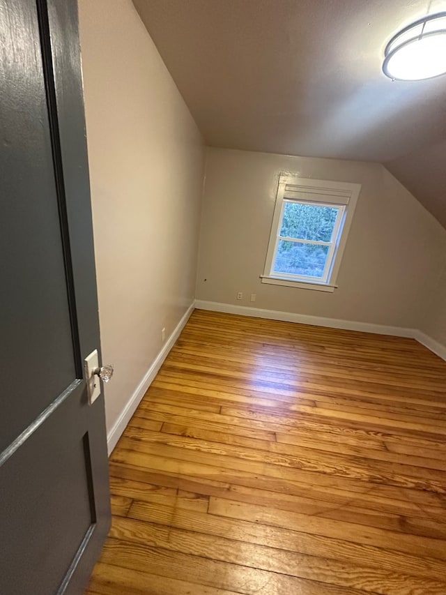 bonus room with light wood-type flooring, vaulted ceiling, and baseboards