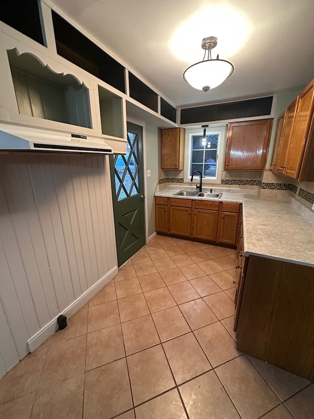 interior space with light countertops, brown cabinetry, light tile patterned floors, a sink, and tasteful backsplash