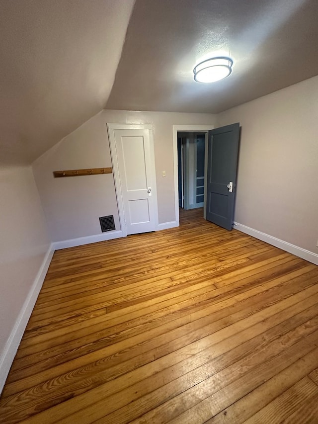 bonus room featuring baseboards, visible vents, vaulted ceiling, and light wood finished floors