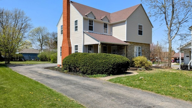 view of front facade with a chimney, a front yard, a shingled roof, and stone siding